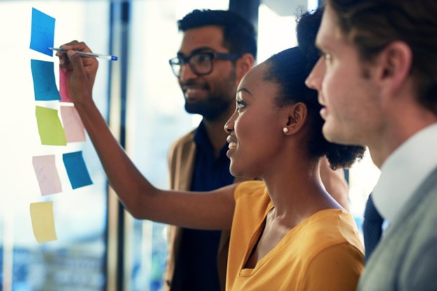 A group of business people is brainstorming and writing their ideas and plans on a glass wall in an office. They are outlining their strategies to achieve future success.