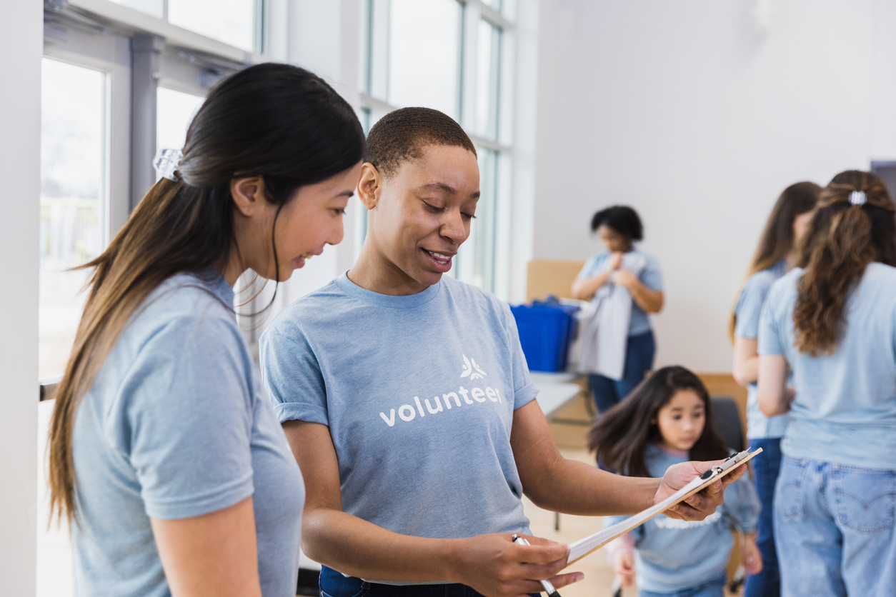 Two female volunteers are reading the loan documents for non-profit organizations while children play and other volunteers work in the background during a clothing drive.